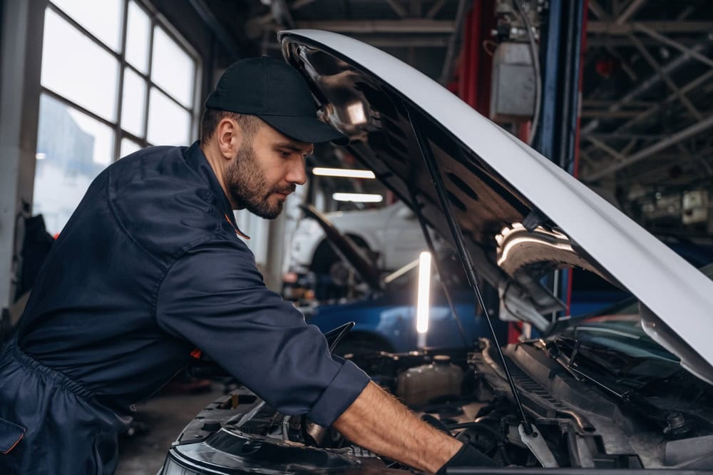 Mechanic leaning into the engine bay of a white car in the shop