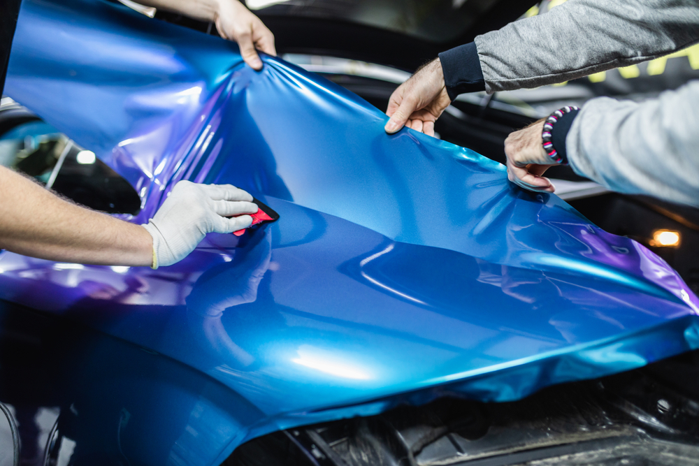 Installers applying a blue color-shift vinyl wrap to a car panel with squeegees