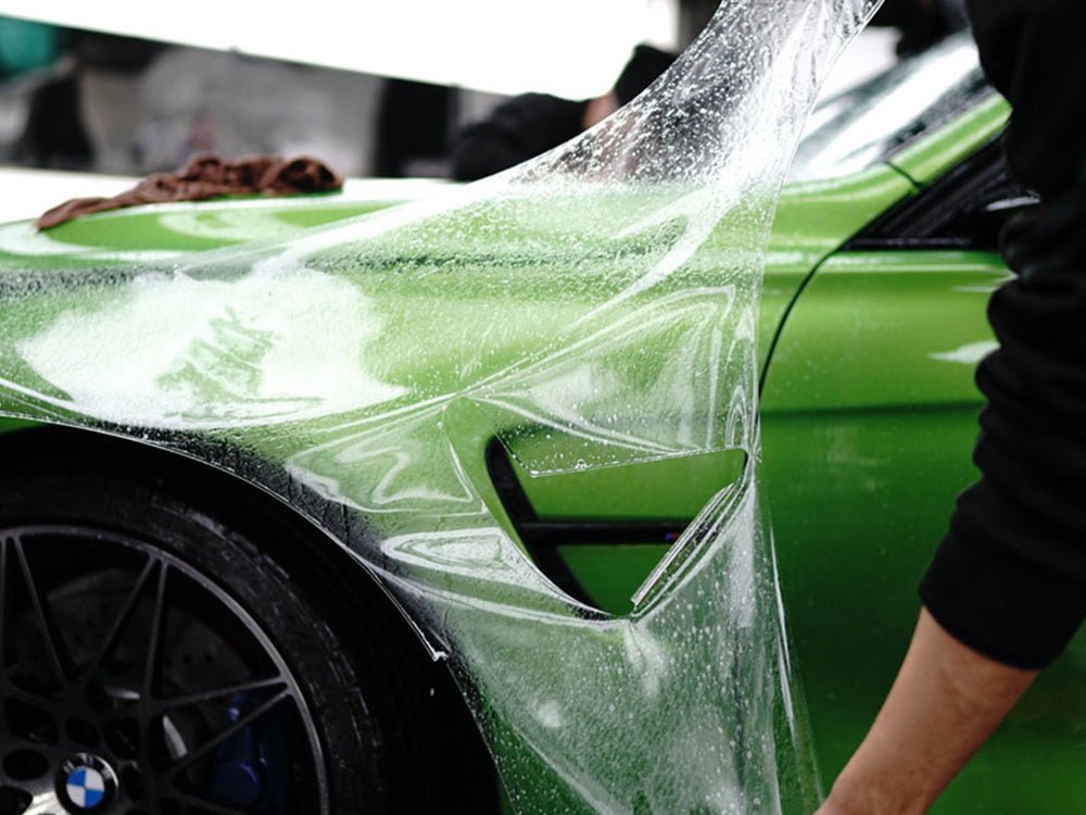 Installer applying pre-cut paint protection film to the fender of a green car