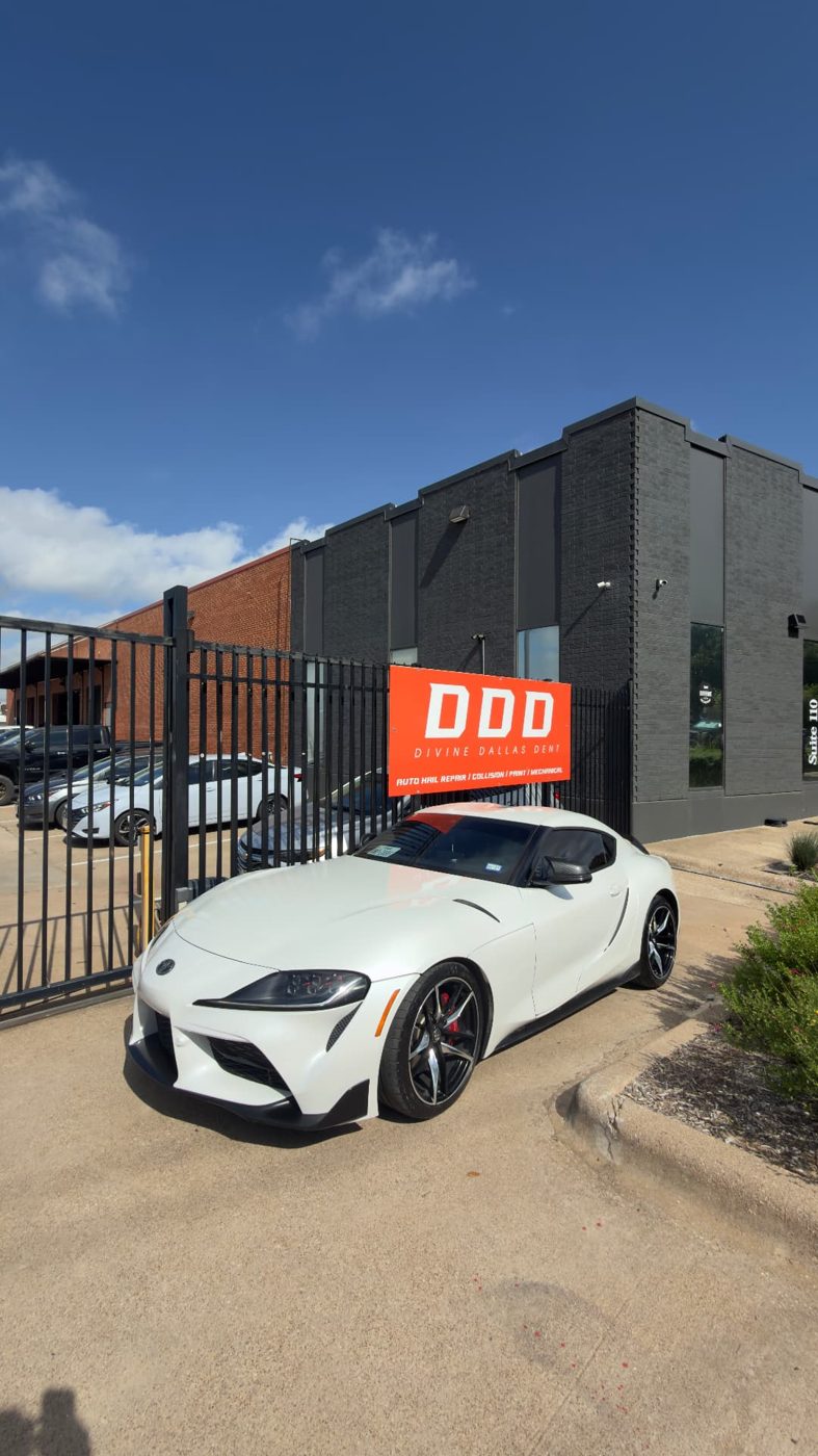 White Toyota Supra parked in front of the Divine Dallas Dent shop sign in Dallas