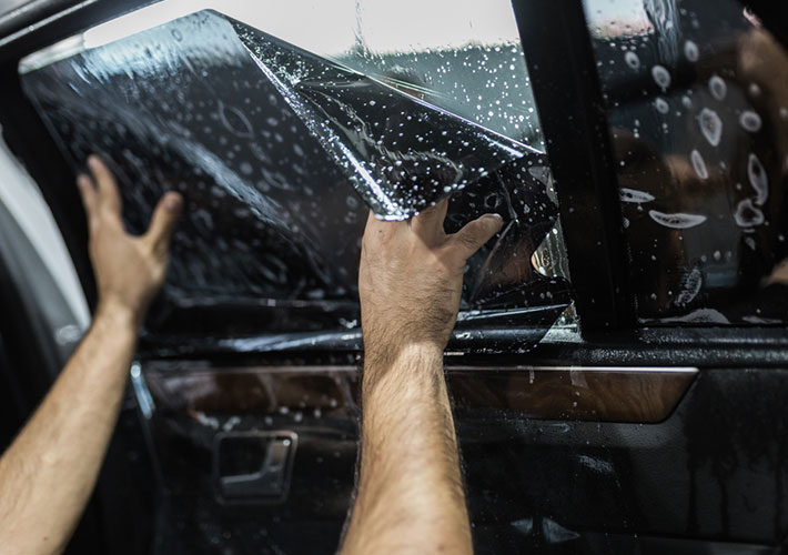 Installer applying dark window tint film to a car door window